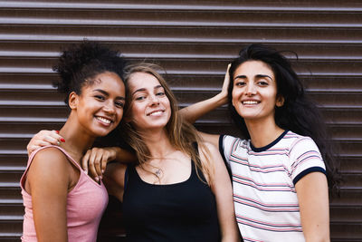 Portrait of female friends smiling while standing by closed shutter