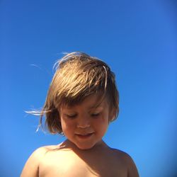 Low angle view of boy against clear blue sky during sunny day