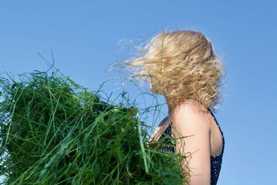 Side view of woman holding grass against blue sky