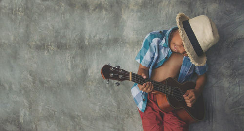 Boy playing guitar against wall