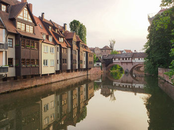 Bridge over river by buildings in city against sky