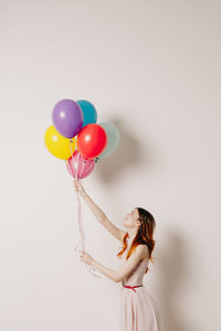 Side view of woman holding colorful balloons against white background