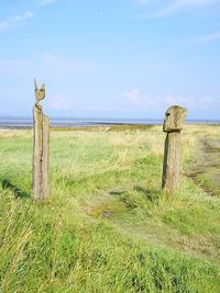 Wooden post on field by sea against sky