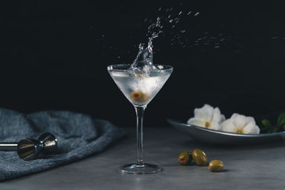 Close-up of olive falling in drink on table against black background