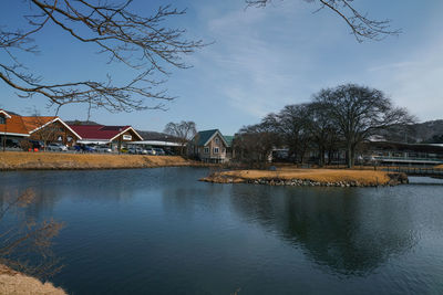 Scenic view of river by houses and trees against sky