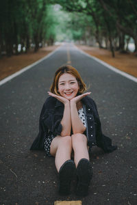 Portrait of a smiling young woman sitting on road