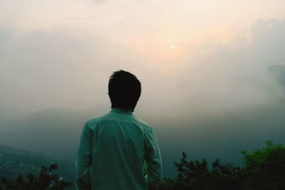 Rear view of man standing against sky in foggy weather