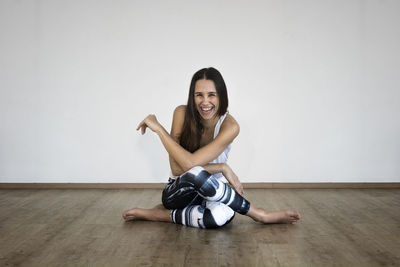 Portrait of smiling young woman sitting on hardwood floor against wall