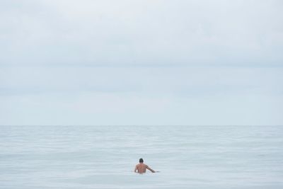 Rear view of shirtless man in sea against sky