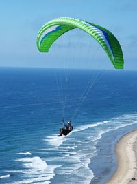 Person paragliding over sea against sky