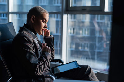 Young man using mobile phone while sitting on window