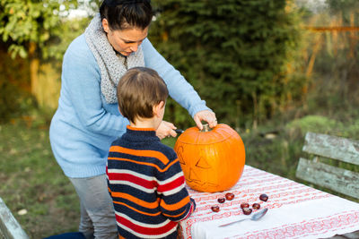 Woman with boy drawing on pumpkin in back yard for halloween