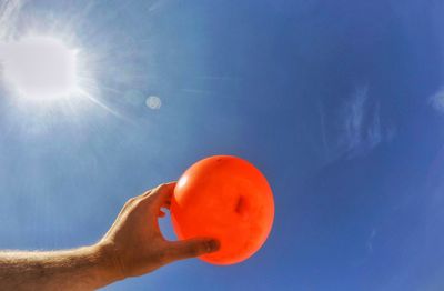 Low angle view of hand holding ball against blue sky