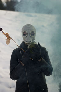 Person in gas mask holding twig during winter