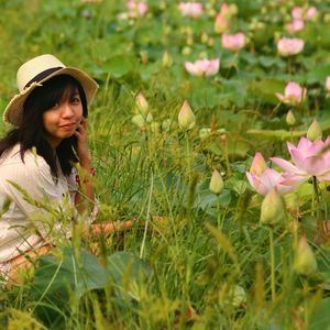 Portrait of smiling woman sitting on grassy field by lotus water lilies