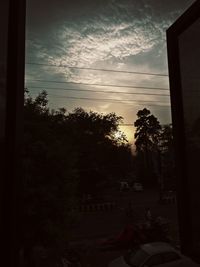 Silhouette trees by city against sky during sunset