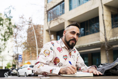 Bearded man sitting outdoors while working over a wooden table