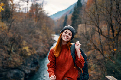 Smiling young woman standing by tree during autumn