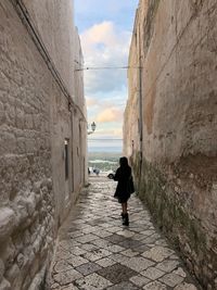 Rear view of woman walking on alley amidst wall