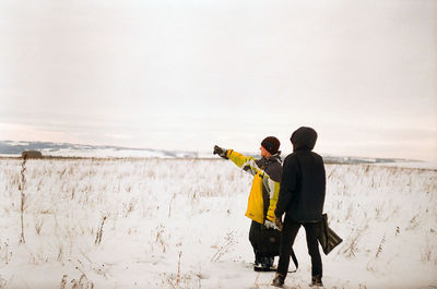 Friends standing on snow covered field against sky