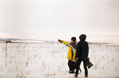 Rear view of men standing on snow covered shore against sky