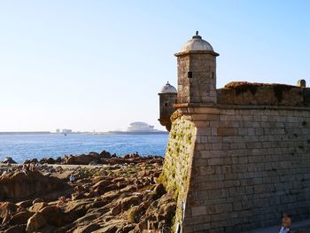 Lighthouse by sea against clear sky