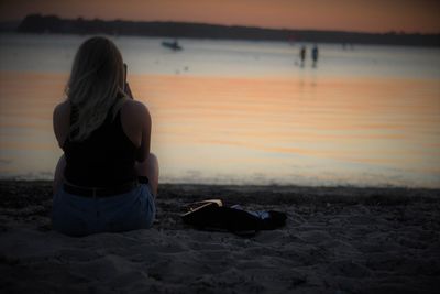 Rear view of woman sitting on beach during sunset