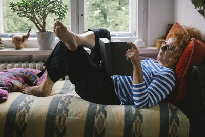 Side view of senior woman reading book while lying on bed at home