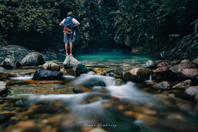 Man standing on rock by river in forest