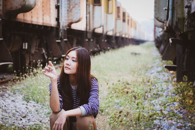 Beautiful young woman holding flower while sitting amidst trains