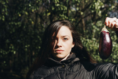 Close-up portrait of young woman holding eggplant against trees