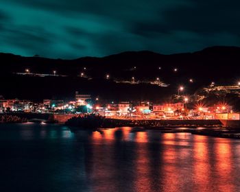 Illuminated city by sea against sky at night