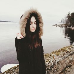 Beautiful young woman in fur coat standing at lakeshore