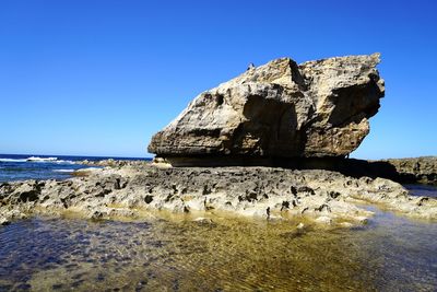 Rock formation on beach against clear blue sky