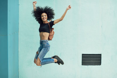 Portrait of happy young backpack woman jumping against wall