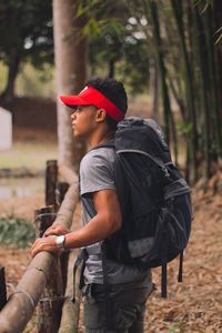 Side view of young man standing against trees