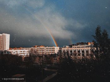 Rainbow over buildings in city against sky at night