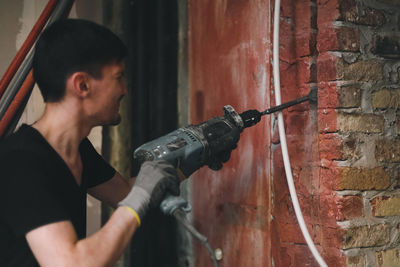 A young man breaks a wall with a perforator.