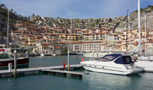 Boats in harbor by buildings in city against sky