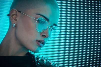 Close-up of young woman with shaved head standing against abstract backgrounds