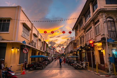 Street amidst buildings in city against sky during sunset