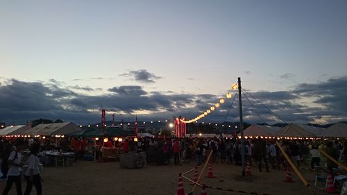 Group of people at illuminated stadium against sky during sunset