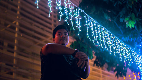 Man standing by illuminated lighting equipment at night