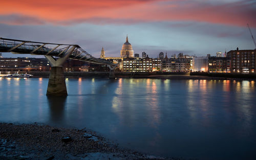 Illuminated bridge over river by buildings against sky in city