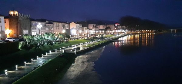 Illuminated buildings by river against sky at night