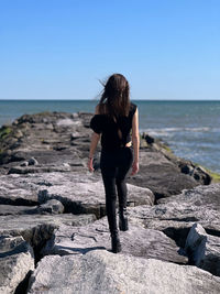 Rear view of woman standing at beach against clear sky