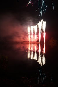 Silhouette of fireworks in lake against sky at night