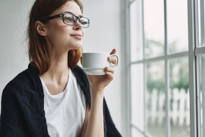 Close-up of woman holding coffee cup by window