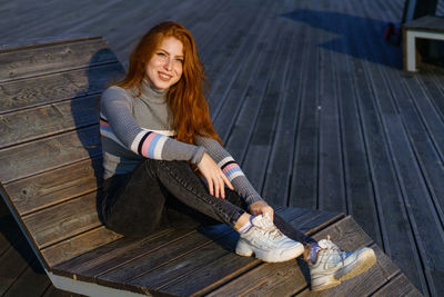 Happy young woman with red hair in the park on wooden flooring