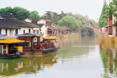 Boats in river by buildings and trees